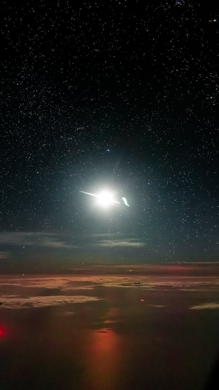 Dramatic night sky featuring a bright full moon and star field reflected on tranquil water.
